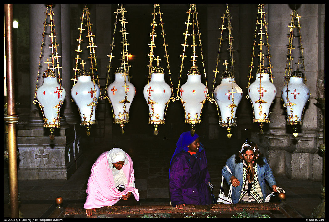 Women worshiping beneath hanging lamps inside the Church of the Holy Sepulchre. Jerusalem, Israel