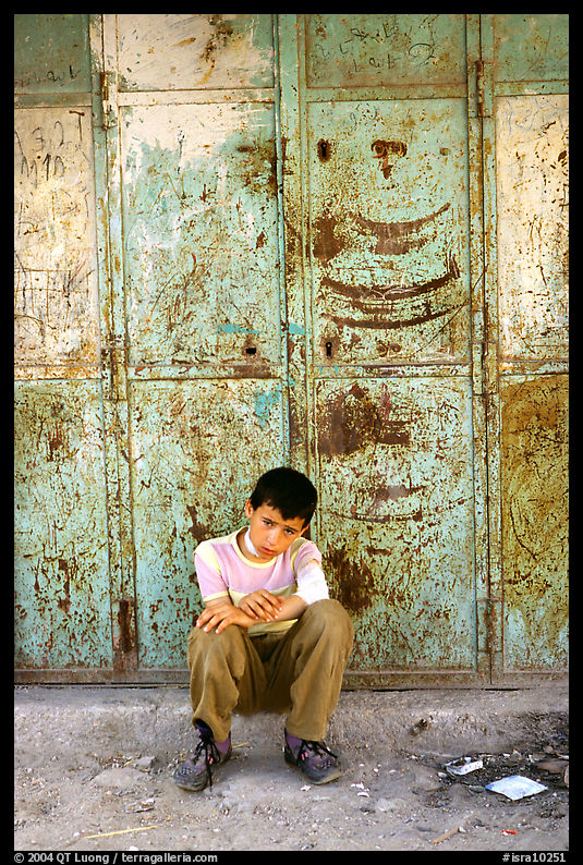 Young boy sitting in front of a closed store, Hebron. West Bank, Occupied Territories (Israel)