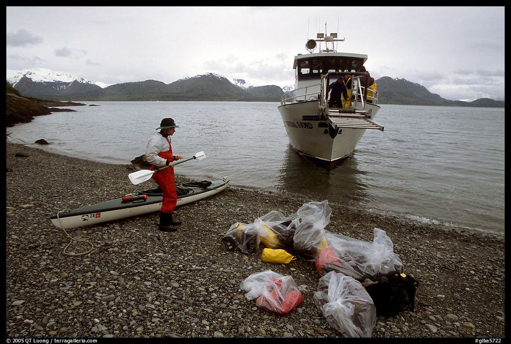 Kayaker standing with gear wrapped in plastic bags after drop-off. Glacier Bay National Park, Alaska