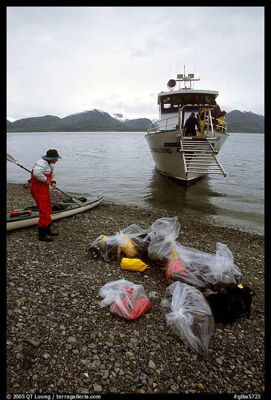 Kayaker standing with gear wrapped in plastic bags after drop-off. Glacier Bay National Park, Alaska