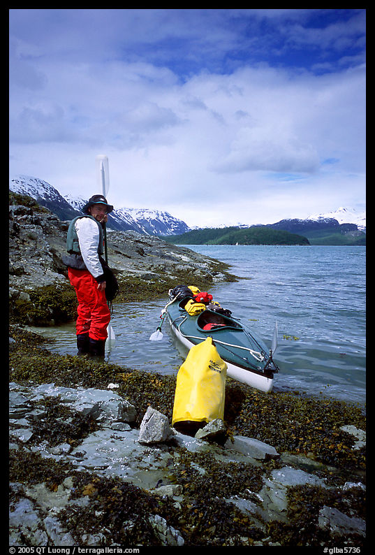 Kayaker standing next to dry bag and kayak on a small island in Muir Inlet. Glacier Bay National Park, Alaska