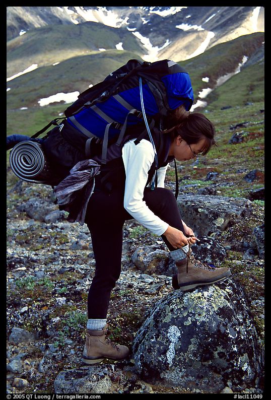 Woman backpacker with a large backpack tying up her shoelaces. Lake Clark National Park, Alaska