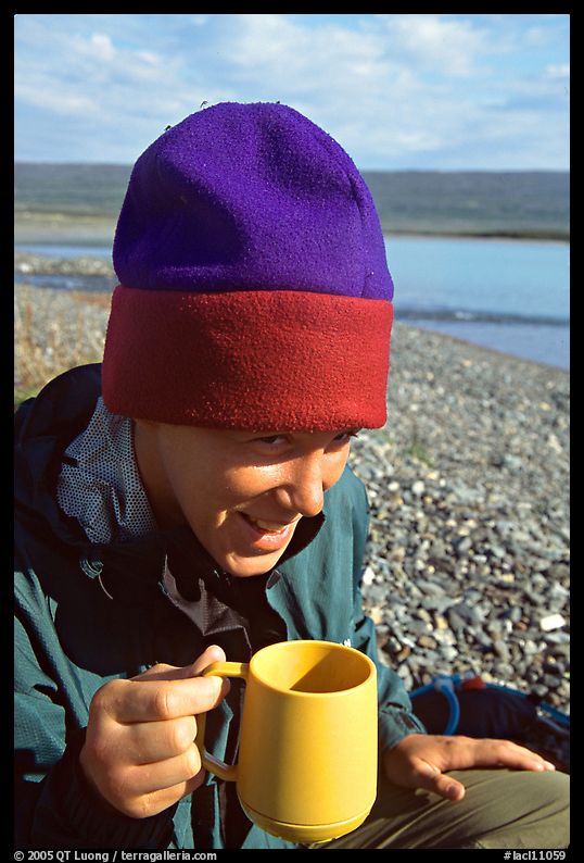 Backpacker drinking from a cup, with mosquitoes on her hat. Lake Clark National Park, Alaska