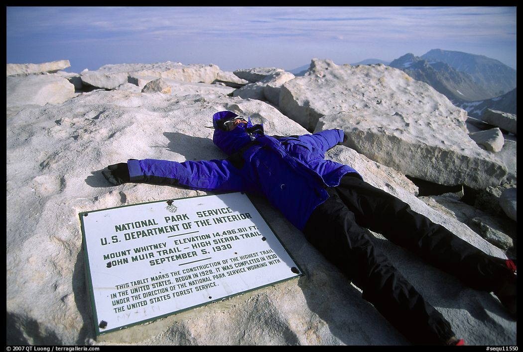 Hiker laying exhausted on Mt Whitney summit sign. Sequoia National Park, California