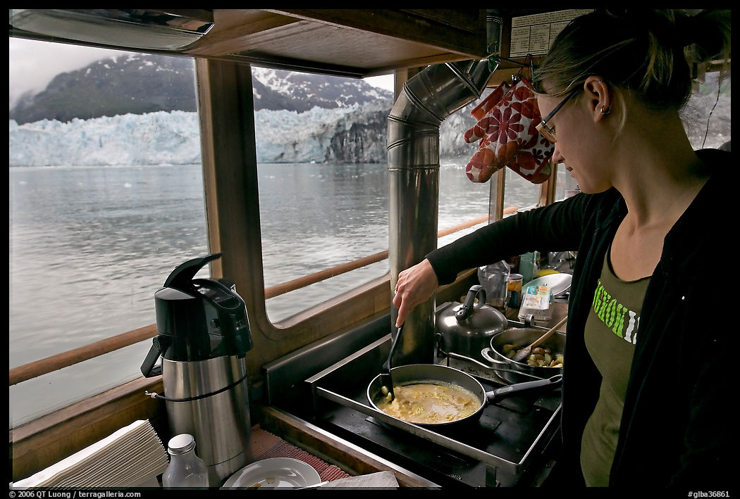 Woman cooking eggs aboard small tour boat, with glacier in view. Glacier Bay National Park, Alaska, USA.
