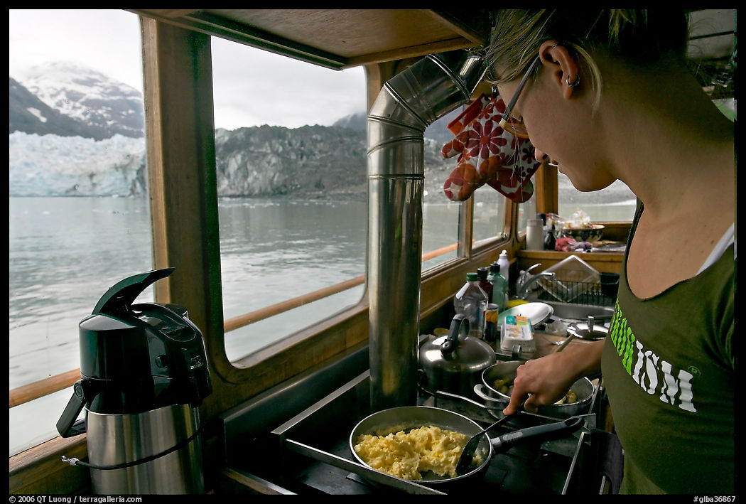 Woman prepares breakfast eggs aboard small tour boat, with glacier in view. Glacier Bay National Park, Alaska, USA.