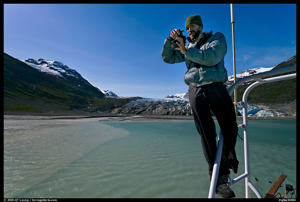 Photographer perched on boat with Reid Glacier behind. Glacier Bay National Park, Alaska, USA.