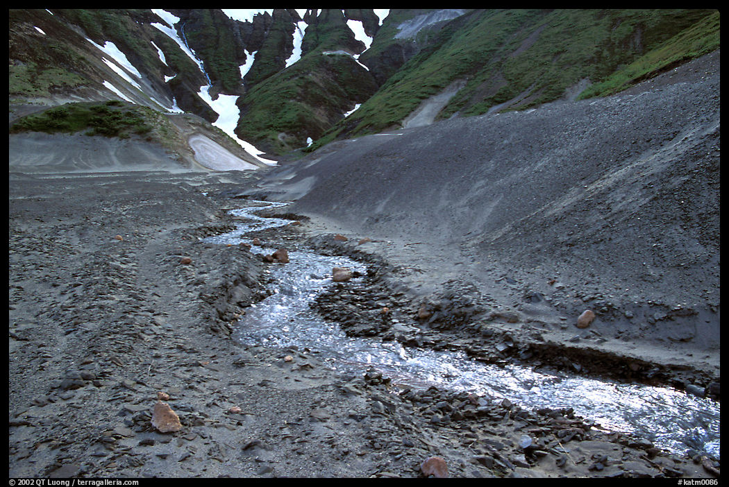 Stream flows from the verdant hills into the barren floor of the Valley of Ten Thousand smokes. Katmai National Park, Alaska, USA.