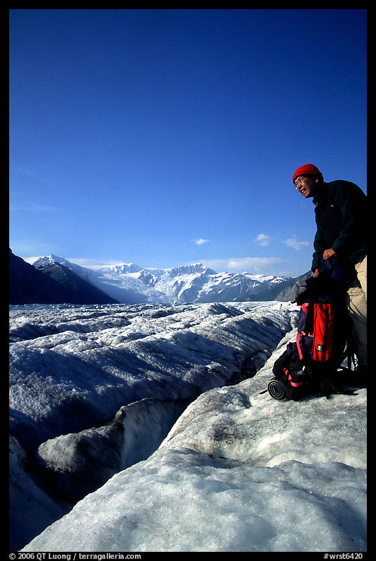 Hiker reaches for item in backpack on Root Glacier. Wrangell-St Elias National Park, Alaska, USA.