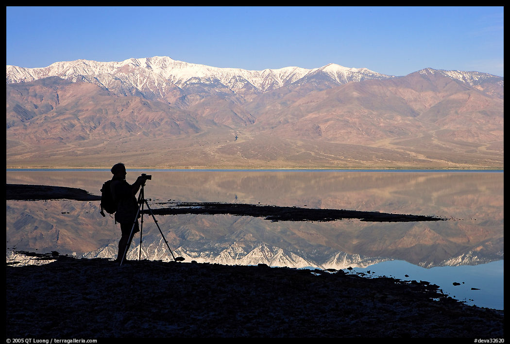 Photographer and Panamint range reflected in a seasonal lake, early morning. Death Valley National Park, California, USA.
