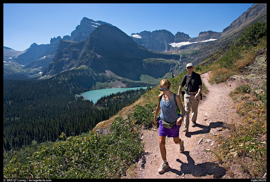 Couple hiking on trail, with Grinnell Lake below. Glacier National Park, Montana, USA.