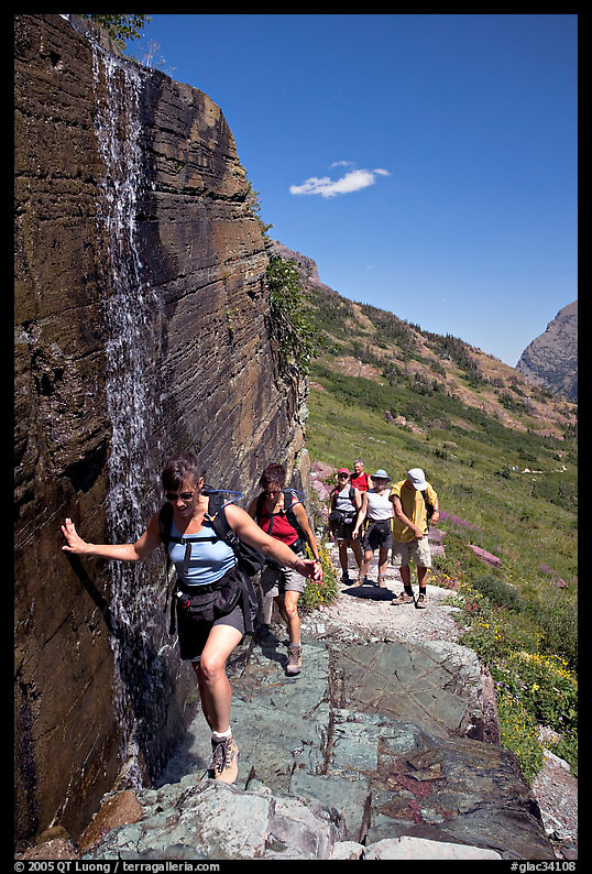 Walking under a small waterfall on the Grinnell Glacier trail. Glacier National Park, Montana, USA.