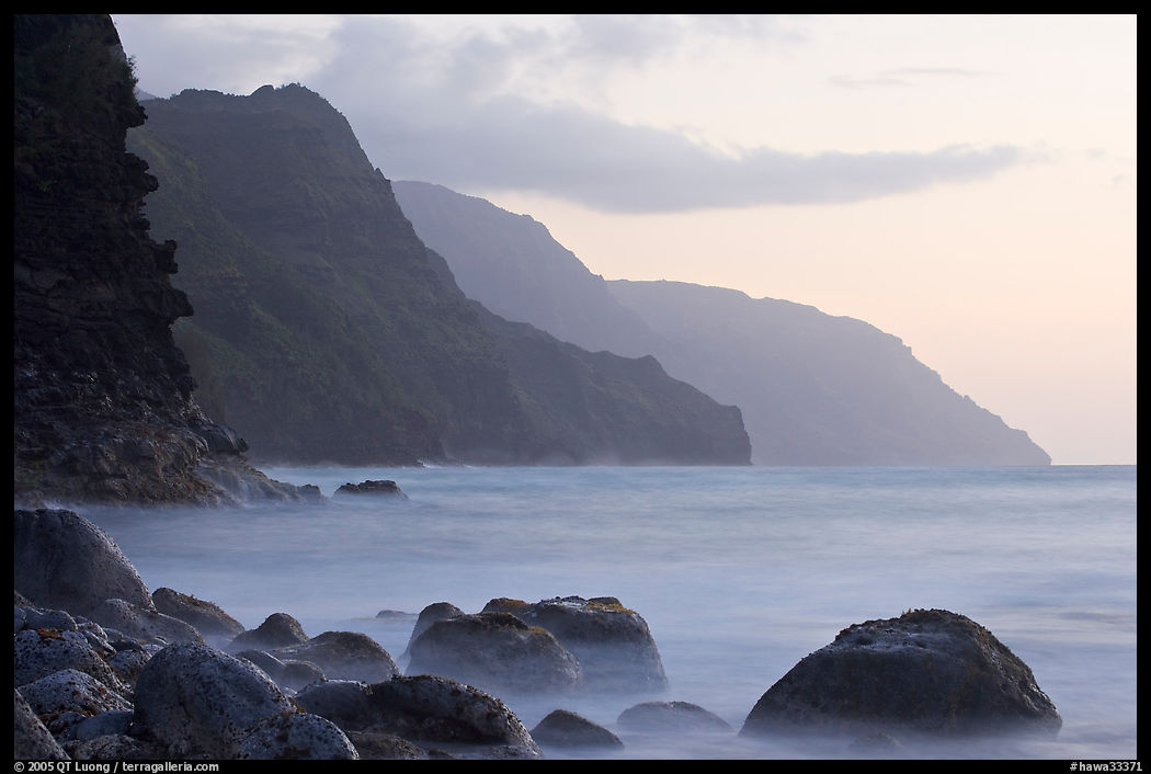 Boulders, surf, and Na Pali cliffs, sunset. Kauai island, Hawaii, USA