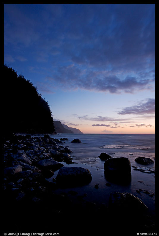 Boulders, surf, and Na Pali cliffs, dusk. Kauai island, Hawaii, USA