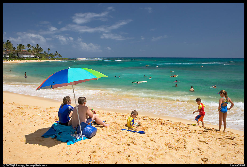Couple sitting under sun unbrella with children playing around, Poipu Beach, mid-day. Kauai island, Hawaii, USA