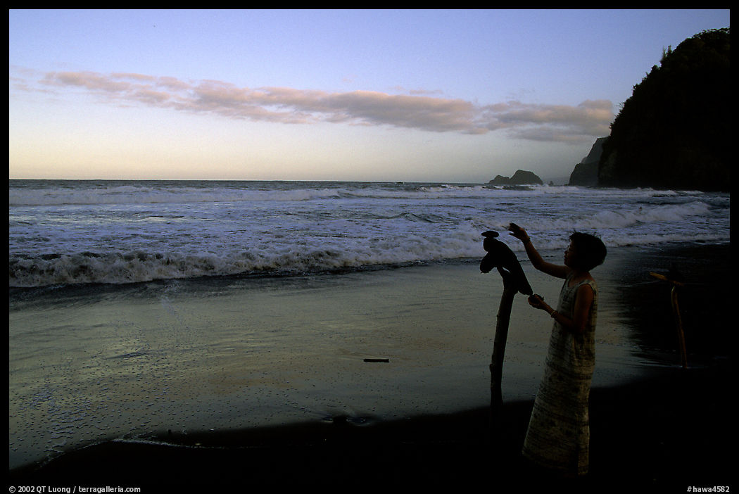 Hawaiian woman piles a stone on a stick as a traditional gesture of reverence, Polulu Beach. Big Island, Hawaii, USA