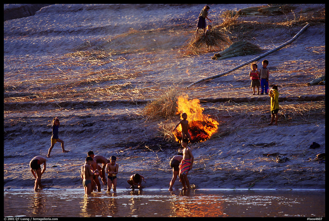 Children bathe in the river and dry out near a fire in a small hamlet. Mekong river, Laos