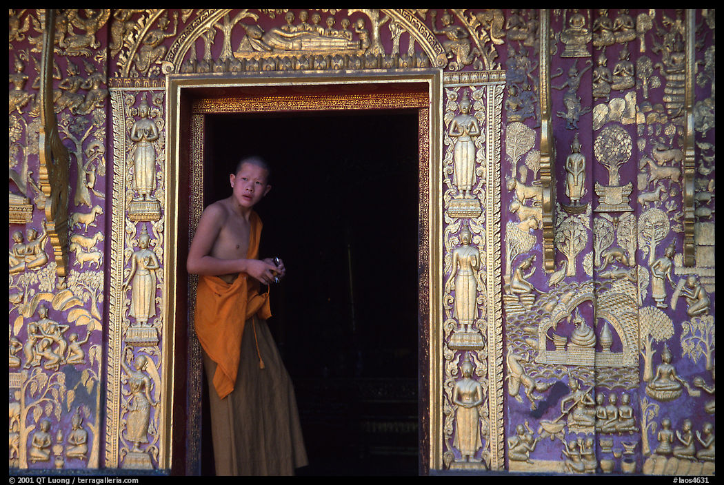 Buddhist novice monk stands at the door of a shrine, Wat Xieng Thong. Luang Prabang, Laos