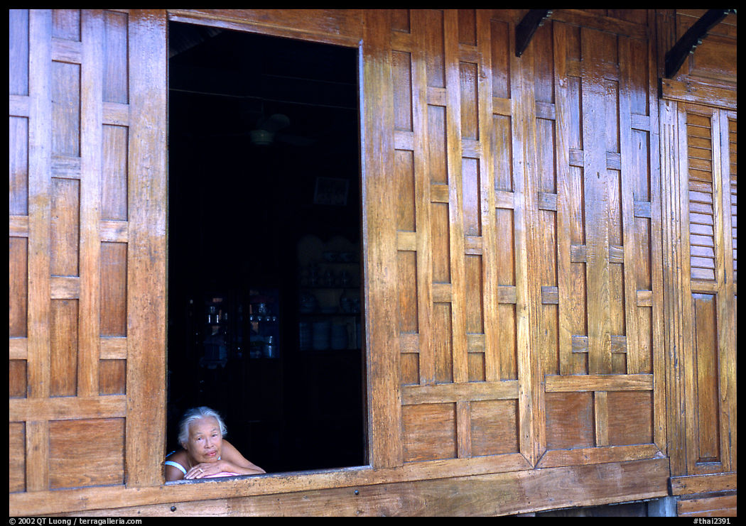 Woman looks out of teak house window. Damonoen Saduak, Thailand