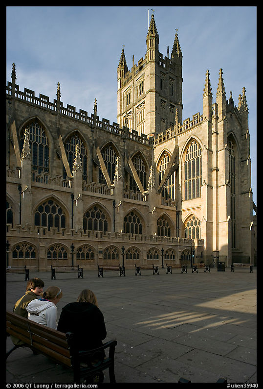 Young people sitting on a bench in a square below Bath Abbey. Bath, Somerset, England, United Kingdom