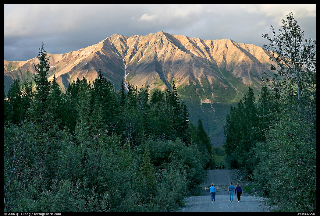 People walking on unpaved road, with last light on mountains. McCarthy, USA
