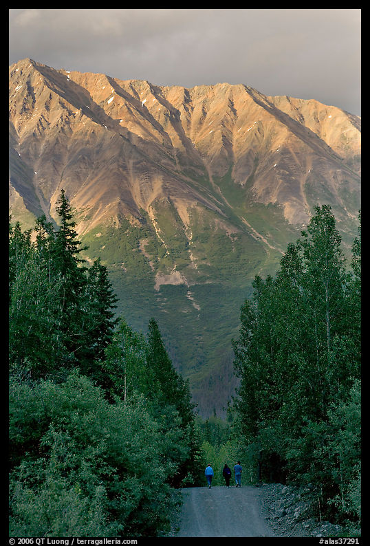 People strolling on unpaved path, with sunset light on mountains. McCarthy, USA