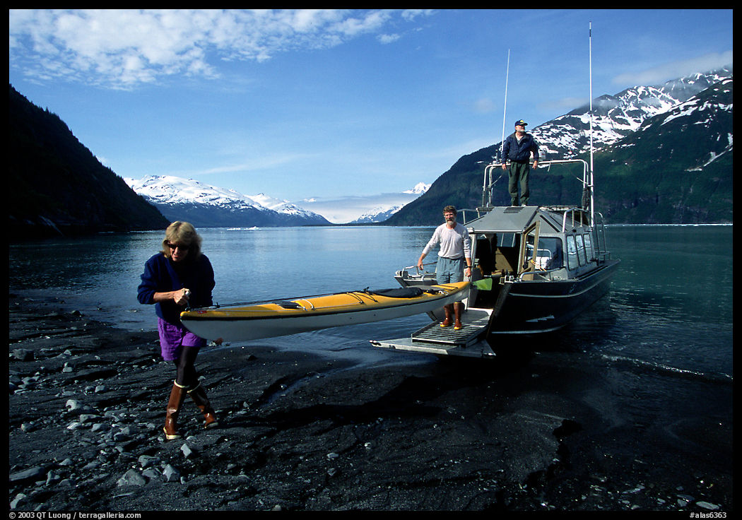 Man and woman carry kayak out of small boat at Black Sand Beach. Prince William Sound, Alaska, USA