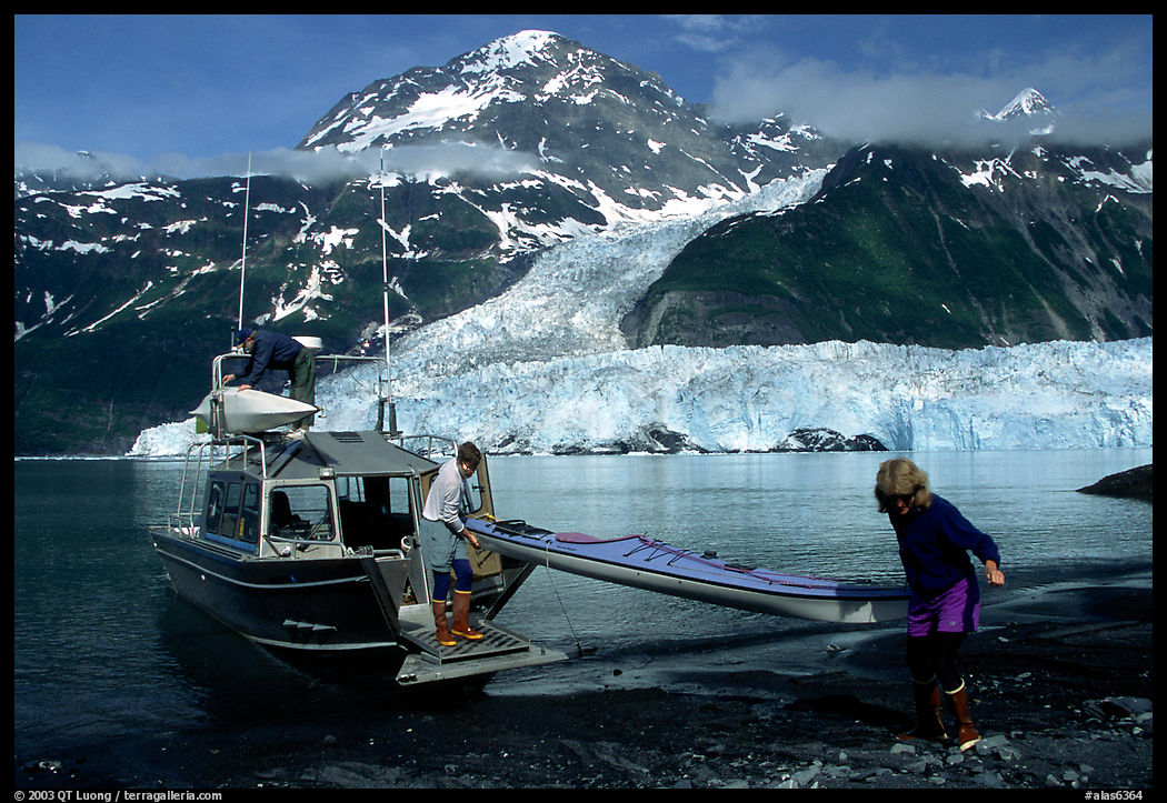 Man and woman  unload  kayak from the water taxi boat at Black Sand Beach. Prince William Sound, Alaska, USA