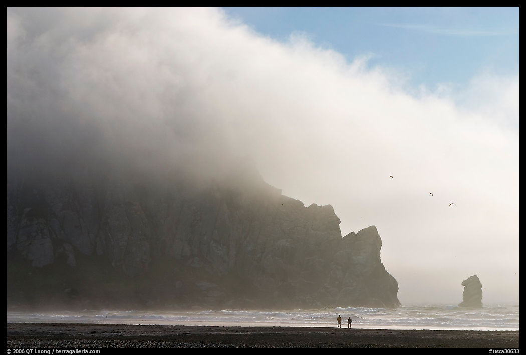 Two people strolling on the beach at the base of Morro Rock. Morro Bay, USA