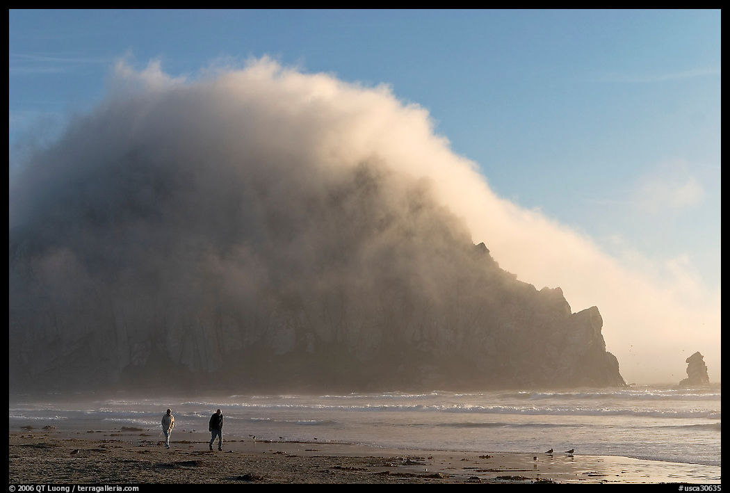 Couple walking on the beach, with Morro Rock and fog behind. Morro Bay, USA