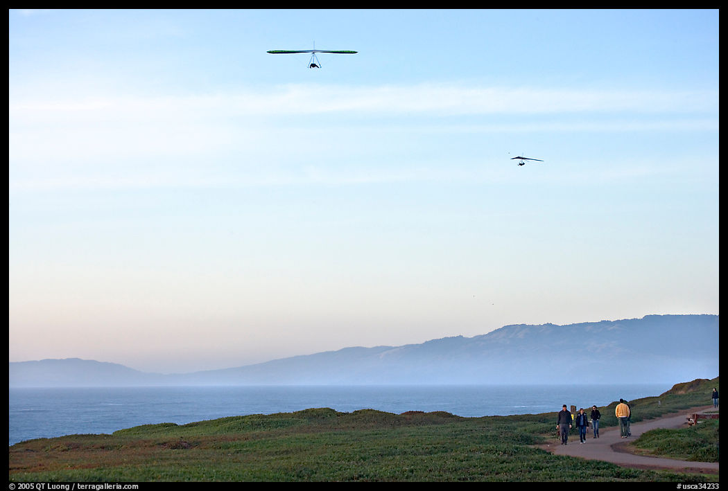 Hang gliders soaring above hikers, Fort Funston, late afternoon. San Francisco, California, USA