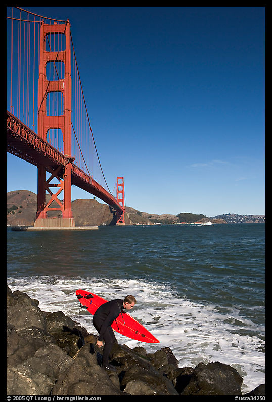 Surfer scrambling on rocks below the Golden Gate Bridge. San Francisco, California, USA