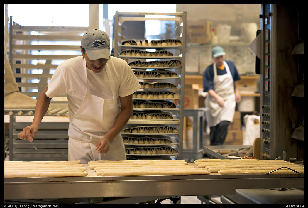 Baker hand-coating lofs of bread. San Francisco, California, USA