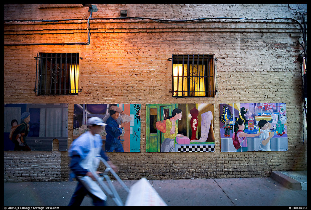 Man pushing a cart in front of mural paintings, Ross Alley, Chinatown. San Francisco, California, USA