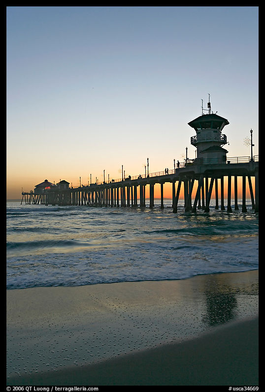 Huntington Pier and reflections in wet sand at sunset. Huntington Beach, Orange County, California, USA