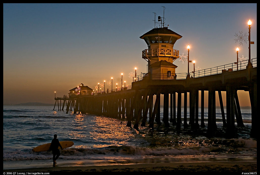 Surfer and Huntington Pier lights at twilight. Huntington Beach, Orange County, California, USA