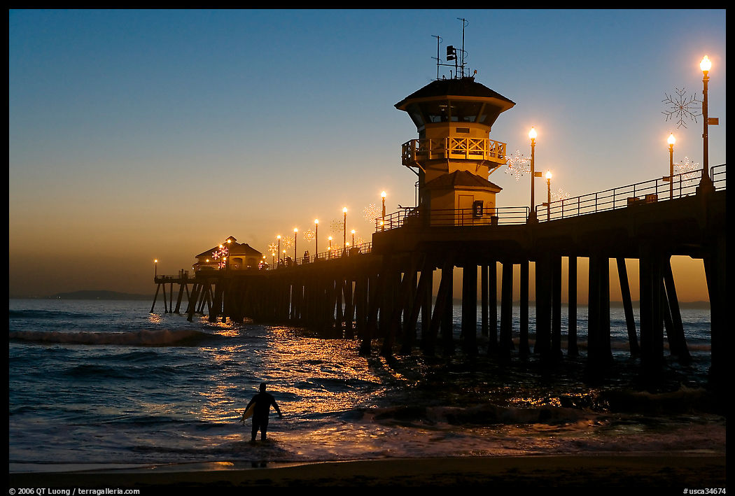 Surfer entering water next to the Huntington Pier, sunset. Huntington Beach, Orange County, California, USA