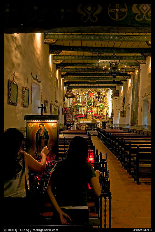 Two women light up candles in the Serra Chapel. San Juan Capistrano, Orange County, California, USA