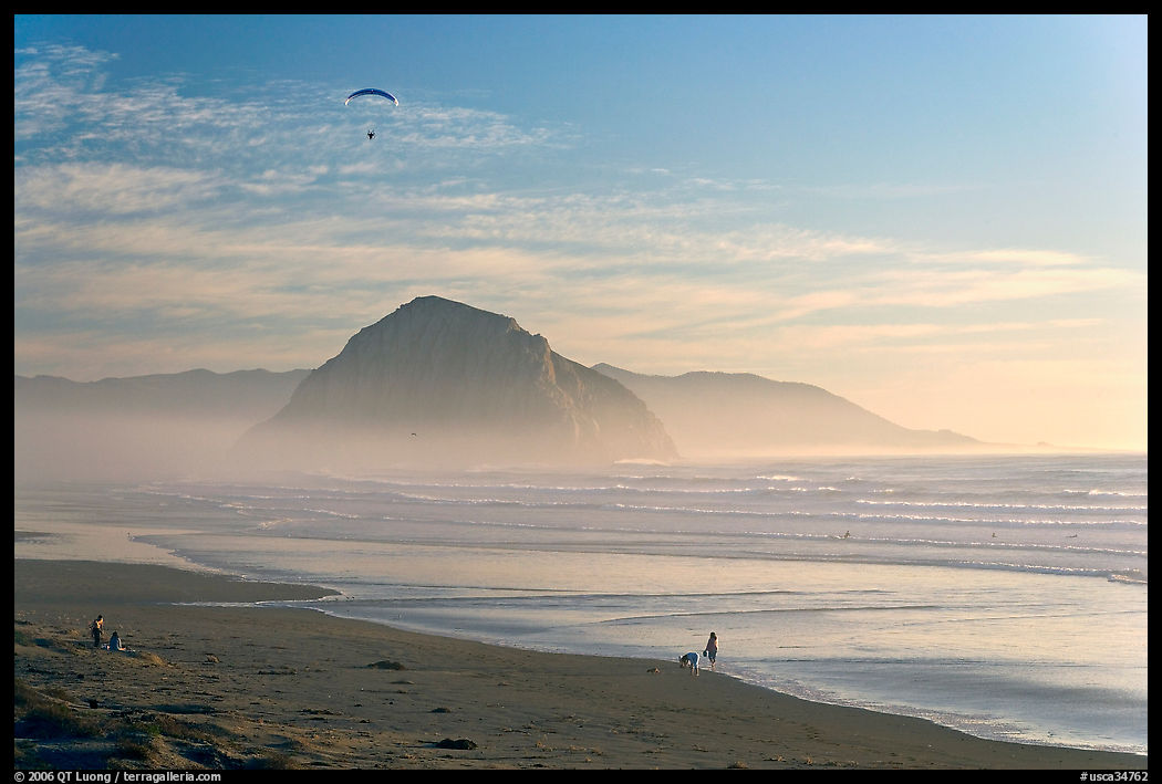 Motorized paraglider, women walking dog, with Morro Rock in the distance. Morro Bay, USA