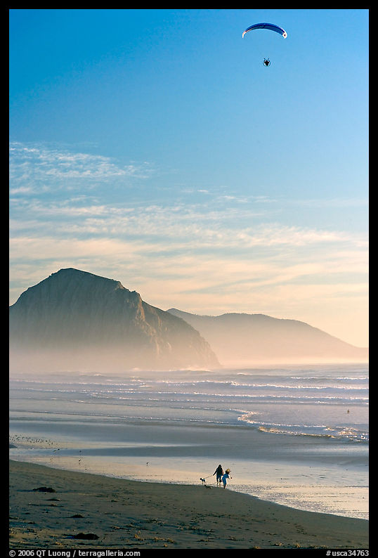 Motorized paraglider, women walking dog, and Morro Rock seen from Cayucos Beach. Morro Bay, USA