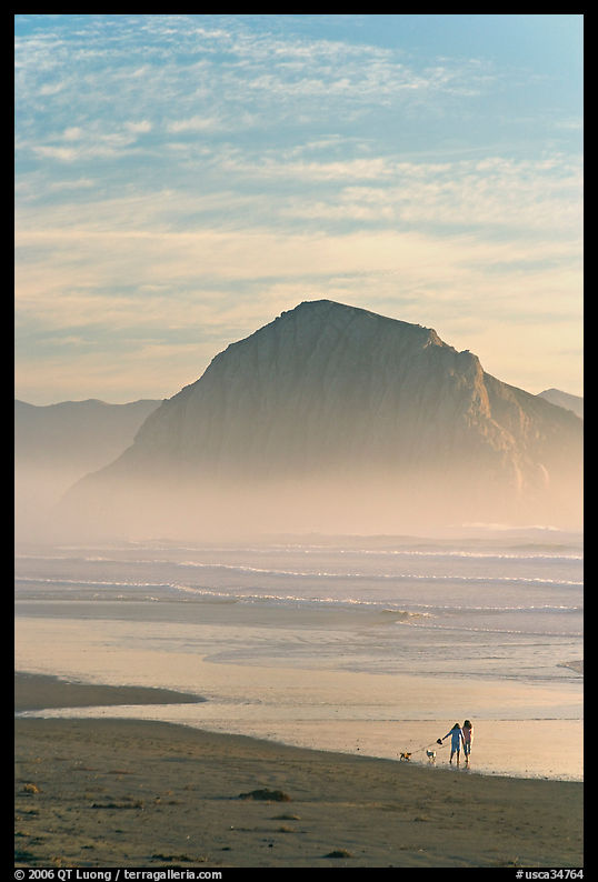 Women walking dog on the beach, with Morro Rock behind. Morro Bay, USA