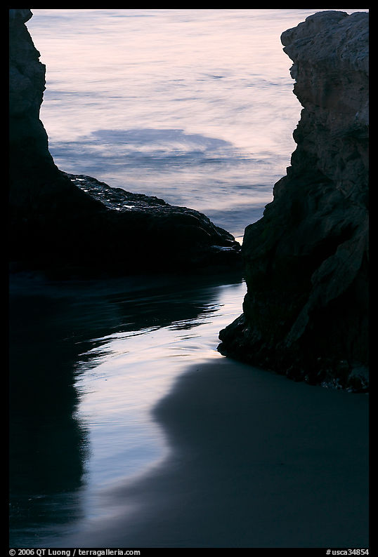 Reflection on wet sand through rock opening, Natural Bridges State Park, dusk. Santa Cruz, California, USA