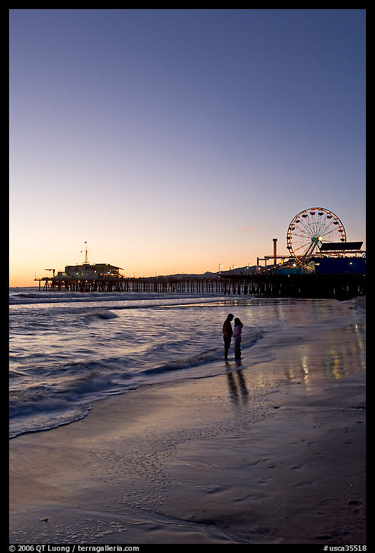 Couple standing on the beach at sunset, with pier and Ferris Wheel behind. Santa Monica, Los Angeles, California, USA