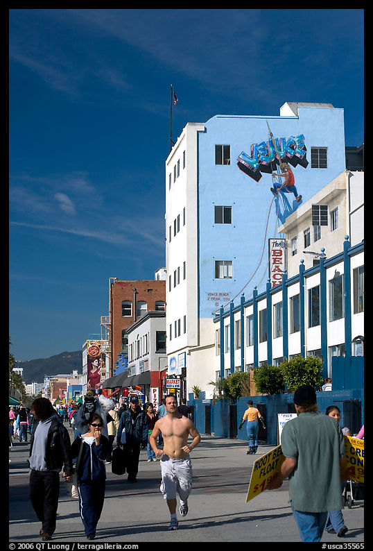 Jogger in the crowd of Ocean Front Walk, with a Venice Mural behind. Venice, Los Angeles, California, USA