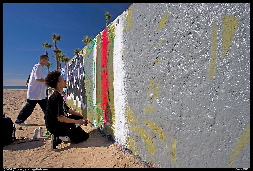 Young men creating graffiti art on a wall on the beach. Venice, Los Angeles, California, USA