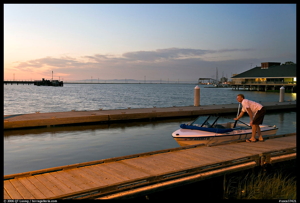 Man holding small boat, Redwood marina, sunset. Redwood City, SF Bay area, California, USA