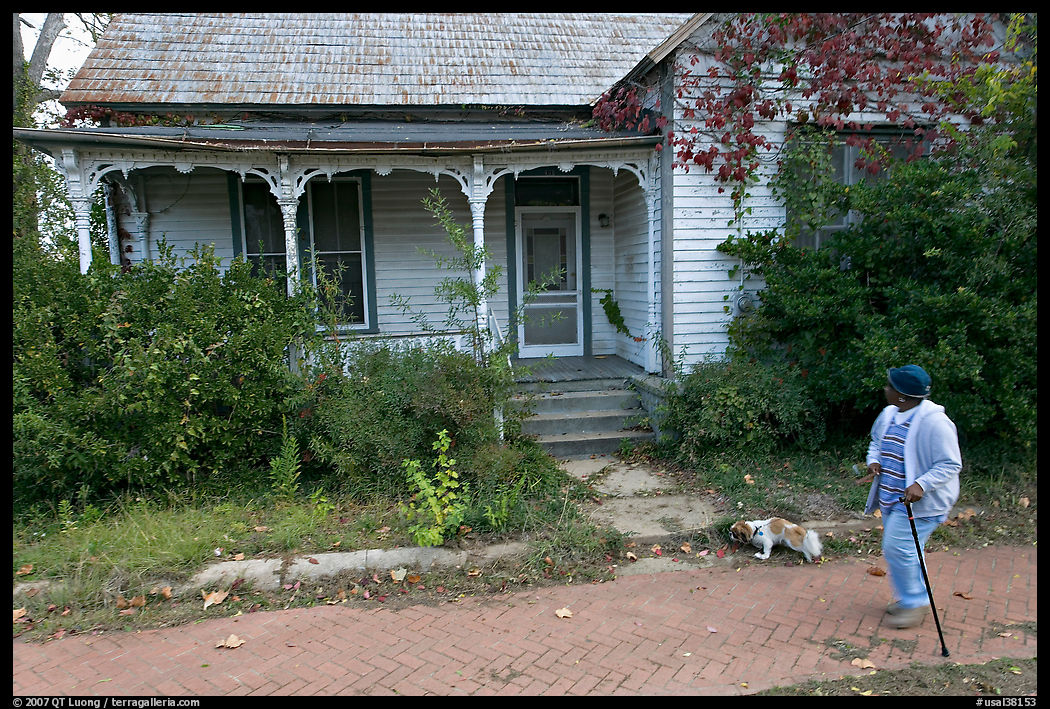 Woman walking dog in front of a crooked house. Selma, Alabama, USA