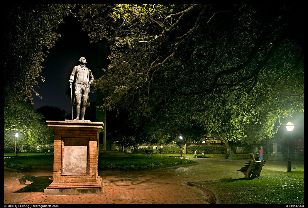 Park with statue and couples sitting on public benches at night. Charleston, South Carolina, USA