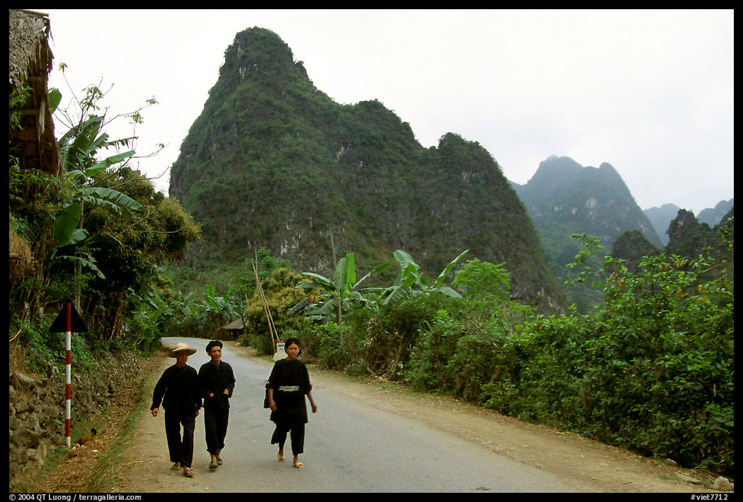 Villagers in traditional garb walking down the road with limestone peaks in the background, Ma Phuoc Pass area. Northeast Vietnam