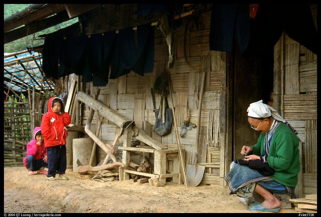 Elderly woman sewing  on her doorstep as kids look up. Northeast Vietnam